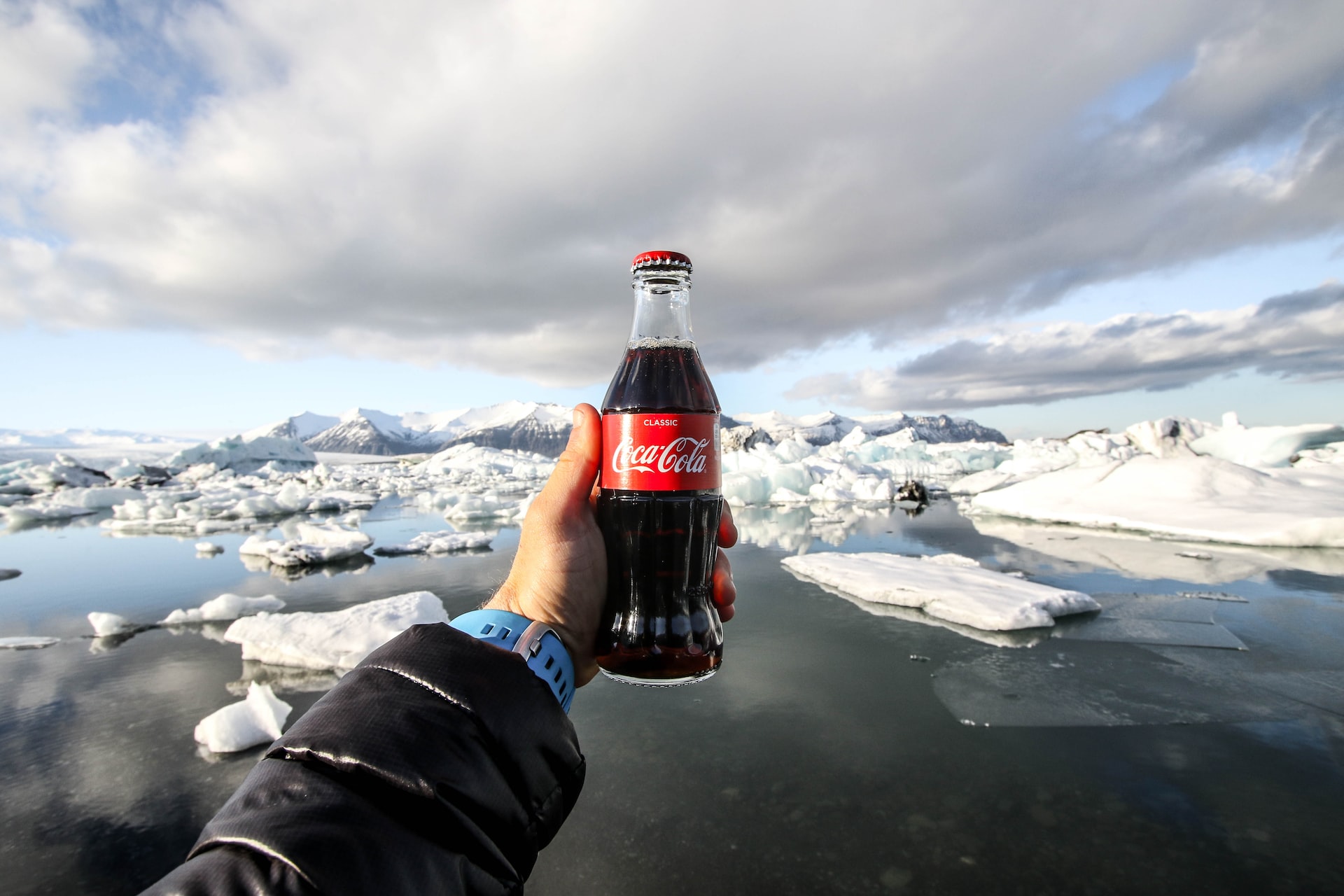 Person holding a glass bottle of Coke out over an arctic vista.