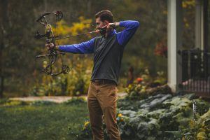 Man drawing compound bow in rainy weather.