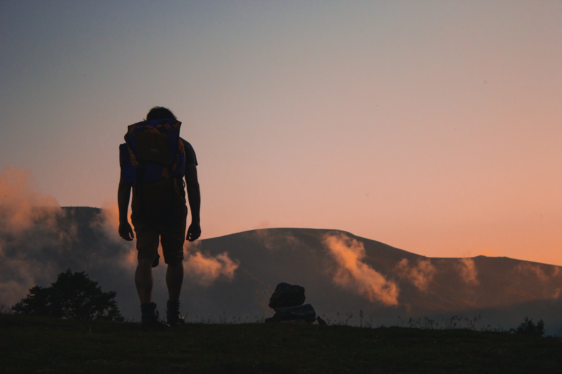 A backpack or on a mountaintop silhouetted by the setting sun.